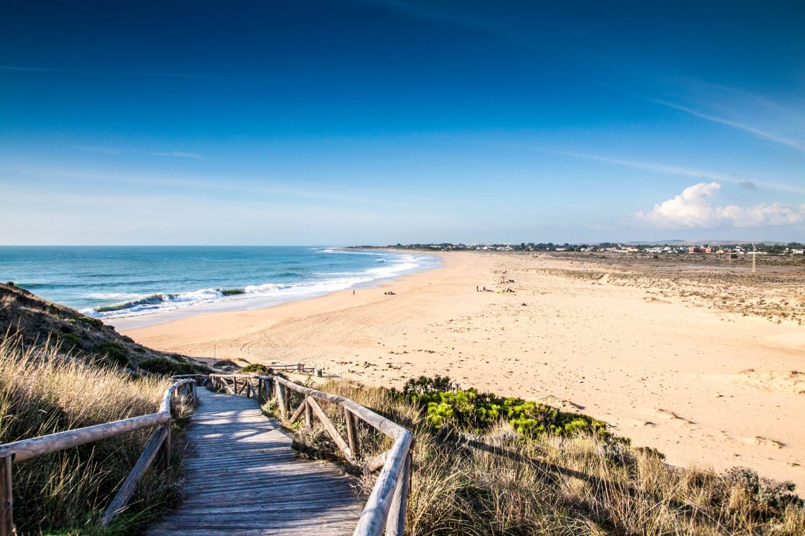 Playa de arena blanca con pasarela de madera que conduce a la playa