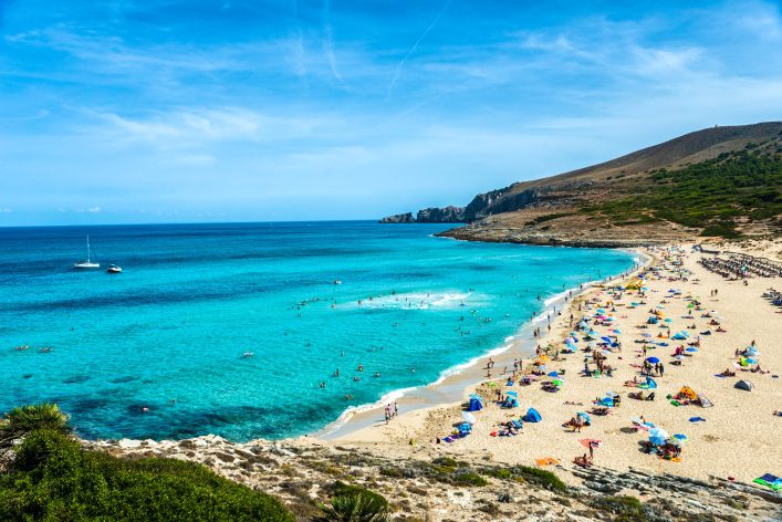 playa de grandes demensiones con bañistas tomando el sol en dia soledo y frente a la playa de aguas cristalinas