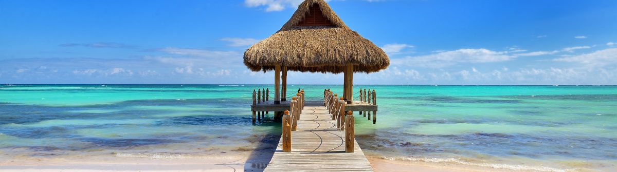 Tropical white sandy beach. Palm leaf roofed wooden pier with gazebo on the beach. Punta Cana, Dominican Republic shutterstock_583369816