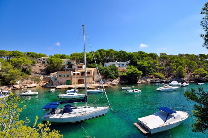 diminito puerto con casas bajas de piedra y pequeñas embarcaciones de epscadores sobre el agua en dia soleado