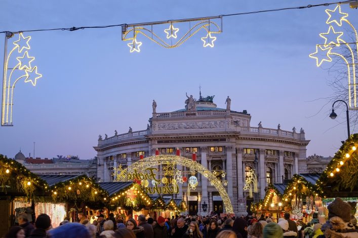 palacio hecho de columnas de piedra con mercado navideño en primer plano y mucha gente